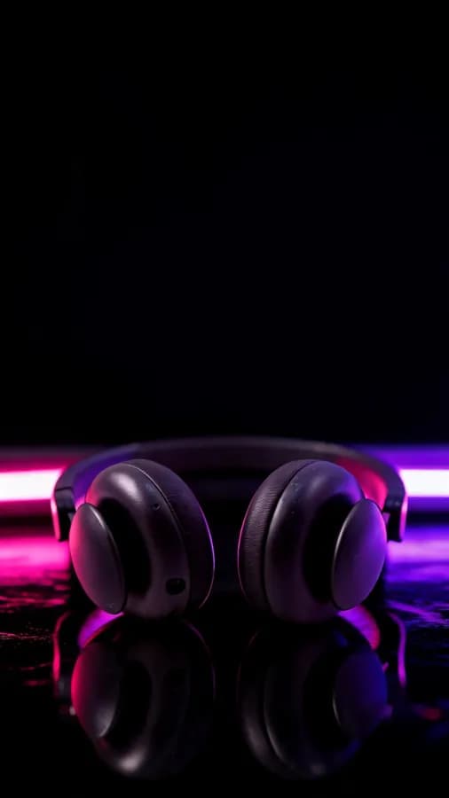 Audífonos negros sobre superficie brillante con luces de neón magenta