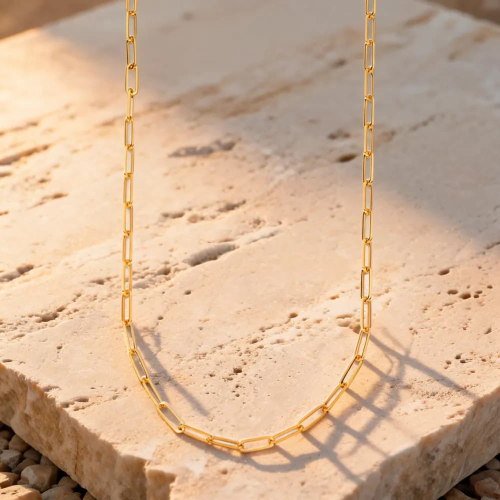 Cadena dorada sobre piedra travertino con luz cálida y sombras marcadas, variación 3